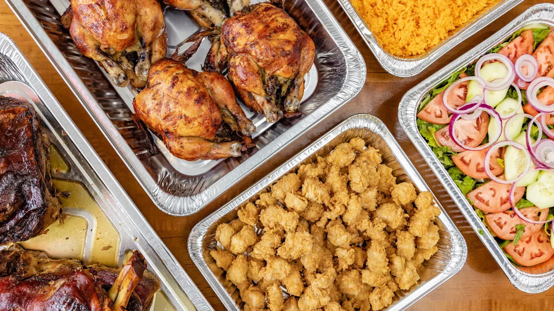 Catering trays of rotisserie chicken, chicharrón, yellow rice and salad